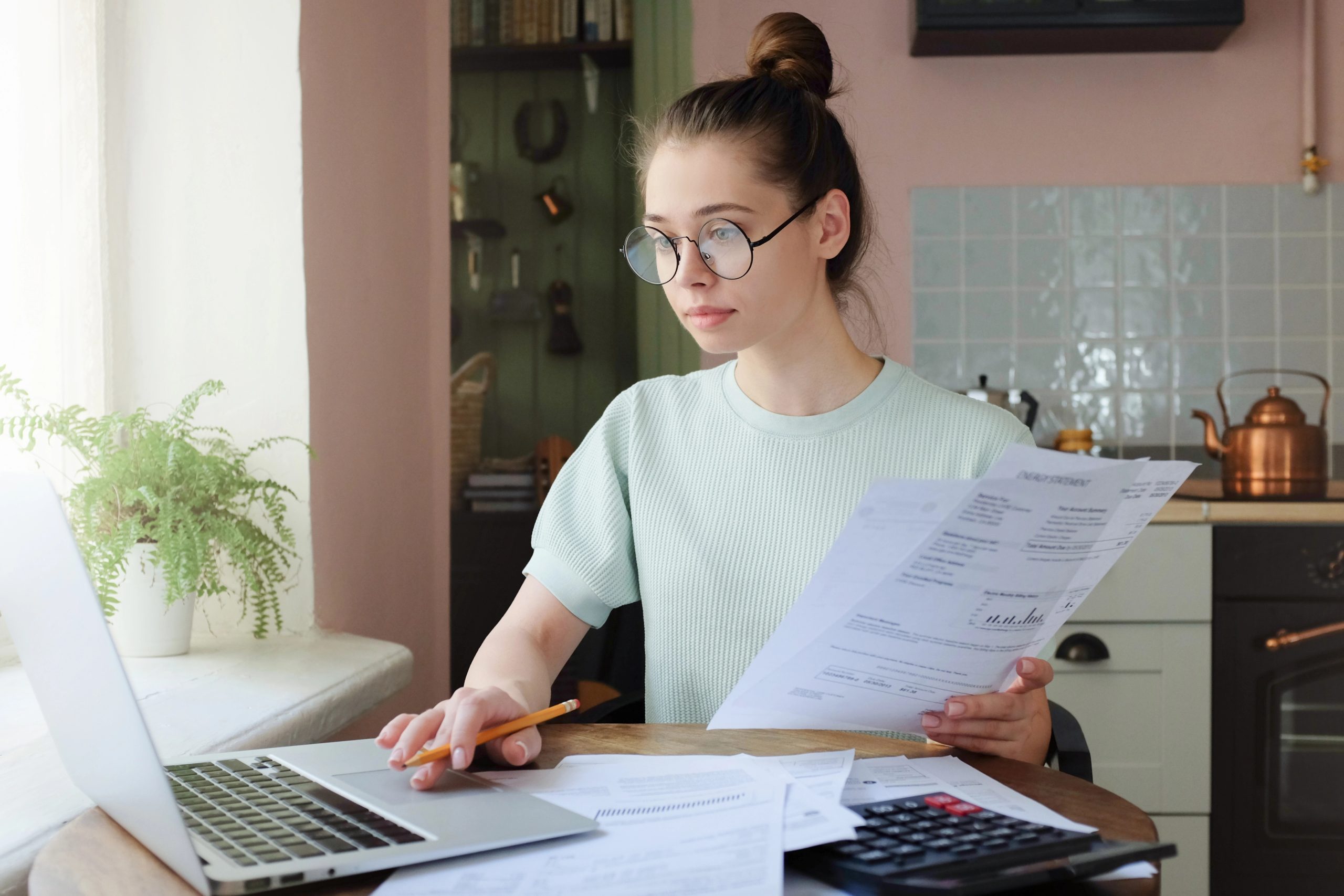 Young woman managing domestic budget, sitting at kitchen