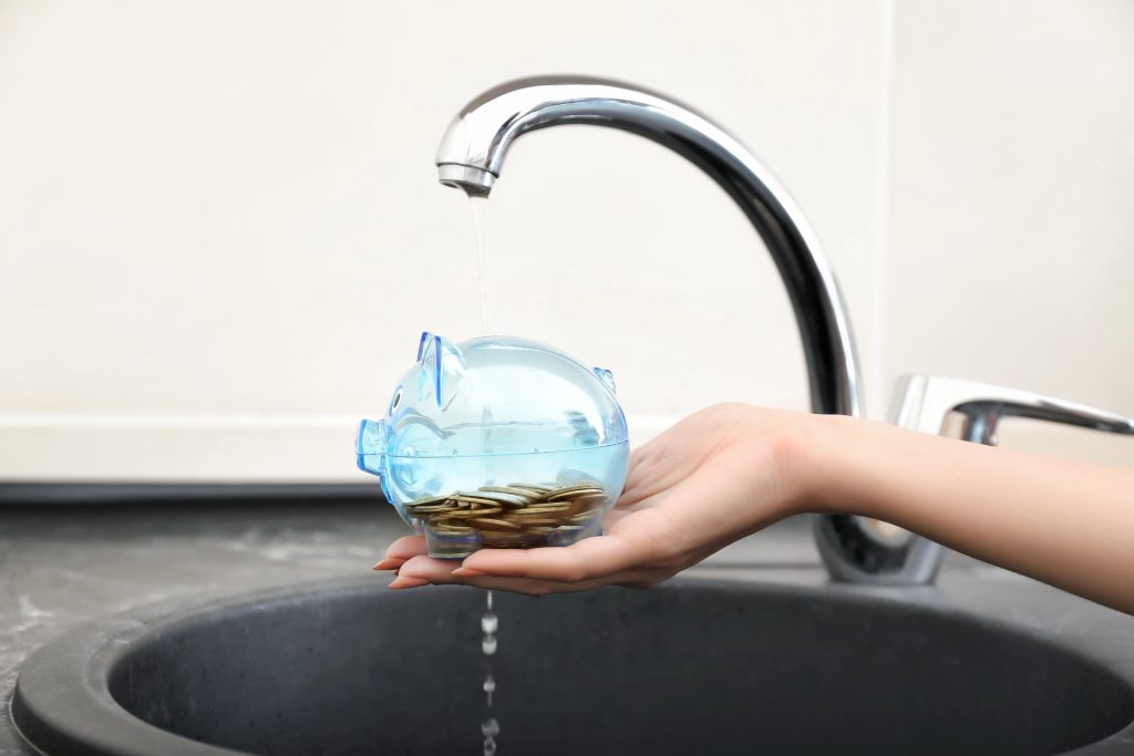 Woman holding piggy bank under metal tap